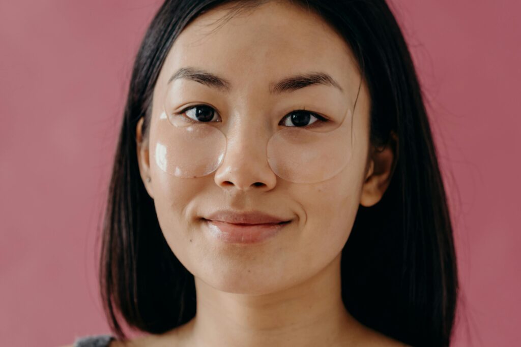 Bí Quyết Sở Hữu Làn Da "Glass Skin" Vạn Người Mê Cùng Mỹ Phẩm Luneria Portrait of an Asian woman with under eye patches against a pink background, embracing self-care and beauty.