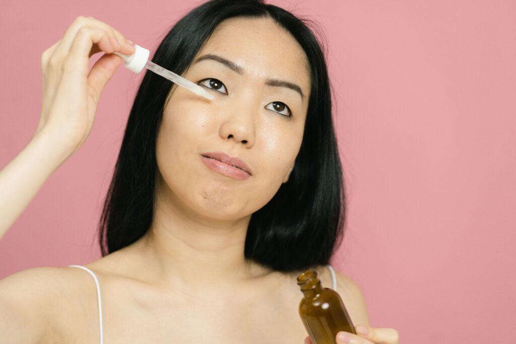 Cập Nhật 5 Xu Hướng Skincare Hàn Quốc Mới Nhất Cùng Mỹ Phẩm Luneria A woman applying facial serum with a dropper for skin care on a pink background.